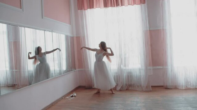 ballerina is training in front of the mirror. A girl in an elegant dress dances ballet in front of a mirror during a lesson in the studio.