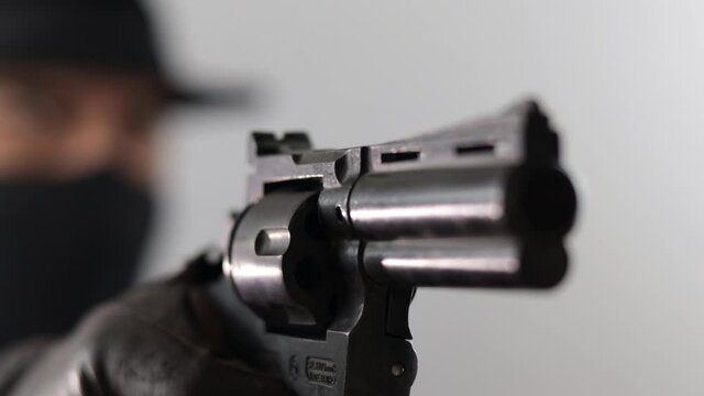 Outlow bandit wearing hat with covered face pointing gun in front. Ciminal concept.