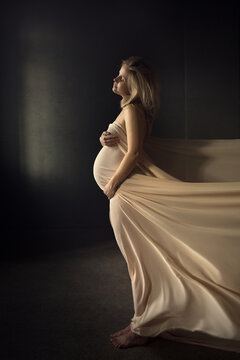 Portrait of beautiful pregnant woman wrapped in piece of fabric in dark room. Image with selective focus, toning and noise effect.