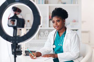 young female doctor recording a lecture on camera, creating video content, consulting a patient...