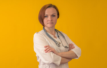 A female doctor with a stethoscope around her neck. It is worth folding his arms on the chest on a yellow background.