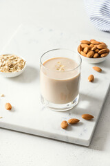 Almond milk in glass and nuts on white background. Close up. Vertical format. Healthy lactose-free beverage. Lack of cholesterol.
