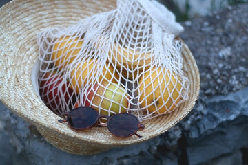 Round retro sunglasses, straw hat and macrame bag filled with various fruits. Selective focus.
