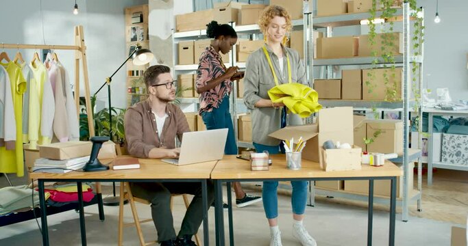 Caucasian and African American young people working in clothing shop Man browsing online on laptop and speaking with female sales manager packing clothes woman employee tapping on tablet Sales concept