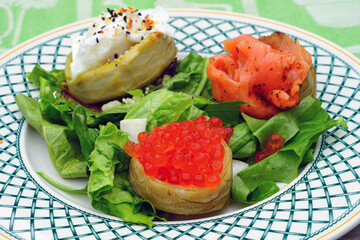 Dish of artichoke bottom topped with smoked salmon, salmon roe and poached eggs over greens
