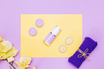 Scented candles, towel,  lotion and orchid flowers on a yellow and purple background.