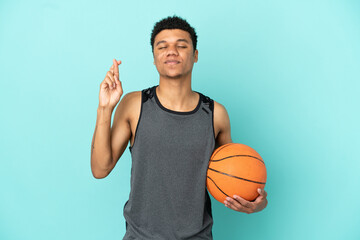 Basketball player African American man isolated on blue background with fingers crossing and wishing the best