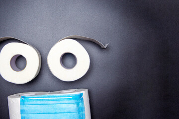 smiley from a medical mask and rolls of toilet paper on a black background. coronavirus panic concept