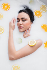young sensual woman taking milk bath with sliced citrus fruits.