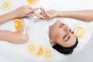 overhead view of young woman relaxing in milky bath with orange and lemon slices.