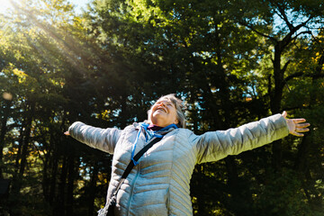 A woman age 60-70 with her arms outstretched to the sky in a forest