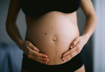 Pregnant woman touching her belly near the windows. Pregnancy and motherhood concept.