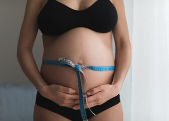 Pregnant woman measure her belly with measure tape. 