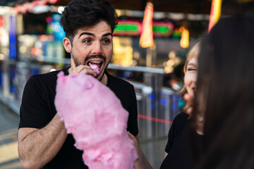 Retrato cercano de chico moreno guapo comiendo algodón de azúcar en zona de atracciones de una feria