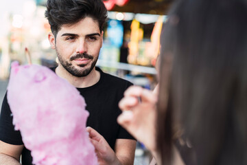 Retrato cercano de chico moreno guapo comiendo algodón de azúcar en zona de atracciones de una feria