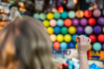 Enfoque selectivo de una mano sujetando un dardo antes de lanzarlo contra globos de colores en una feria