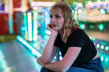Chica joven guapa y rubia sentada en zona de atracciones de una feria