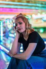 Chica joven guapa y rubia sentada en zona de atracciones de una feria