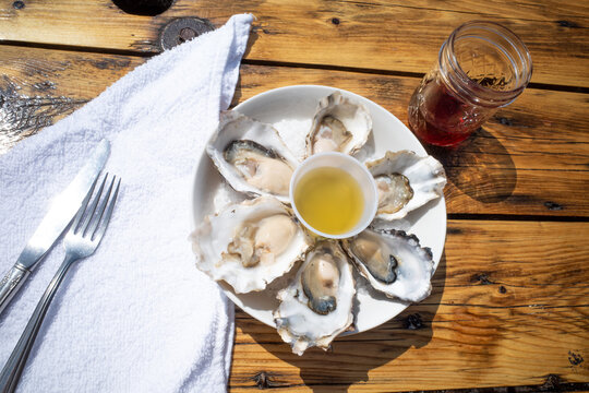 Raw oysters and wine on a wooden table outdoors in bright sunshine