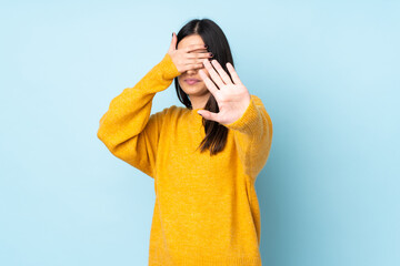 Young caucasian woman isolated on blue background making stop gesture and covering face
