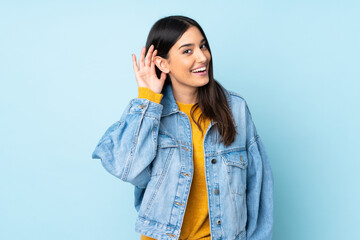 Young caucasian woman isolated on blue background listening to something by putting hand on the ear - obrazy, fototapety, plakaty
