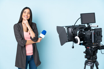 Reporter woman holding a microphone and reporting news isolated on blue background smiling
