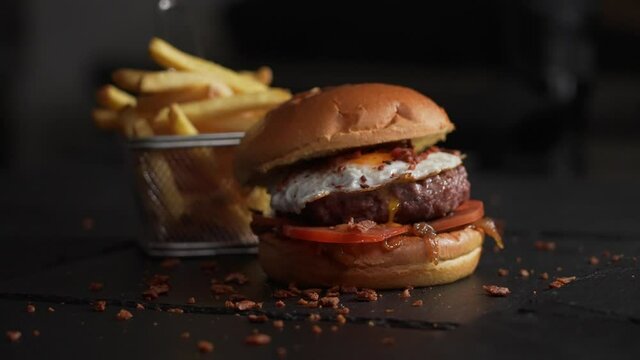 Big American burger menu with egg in slow motion. French fries in the dark background.