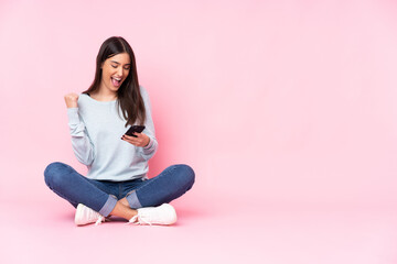 Young caucasian woman isolated on pink background with phone in victory position