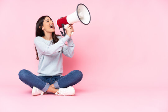 Young caucasian woman isolated on pink background shouting through a megaphone