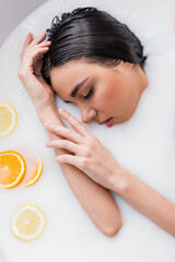 young woman with closed eyes relaxing in milk bath with sliced orange and lemon.