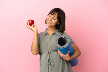 Woman over isolated background pregnant holding an apple and going to yoga classes
