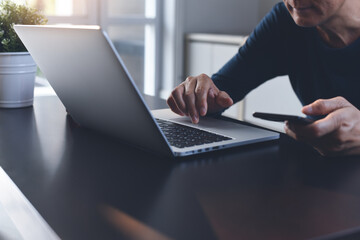 Casual business man freelancer surfing the internet on laptop computer and using mobile phone at home office