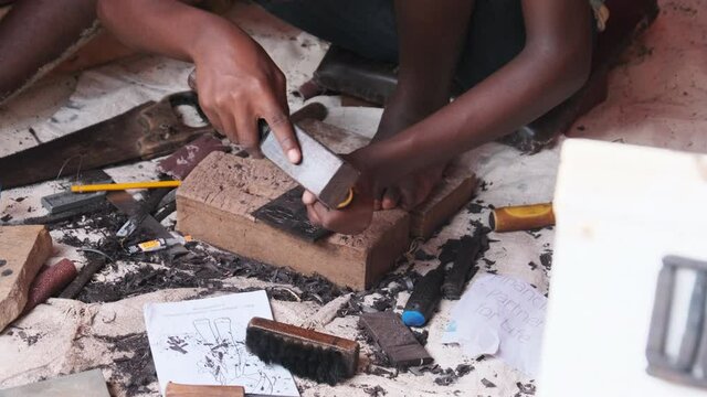 Local African makes hand-made souvenirs at the tourist market, Zanzibar. Close-up of hands with a chisel carving out figures on a tree. African artisan at work. Wood carving is traditional handicraft