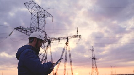 Silhouette of engineer standing on field with electricity towers. Electrical engineer with high...