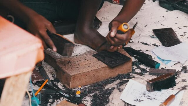 Local African makes hand-made souvenirs at the tourist market, Zanzibar. Close-up of hands with a chisel carving out figures on a tree. African artisan at work. Wood carving is traditional handicraft