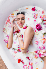 Obraz na płótnie Canvas young woman with closed eyes enjoying floral bath with milk.