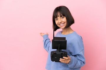 Young mixed race woman holding a drone remote control isolated on pink background extending hands to the side for inviting to come