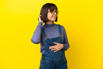 Young pregnant woman over isolated yellow background having doubts
