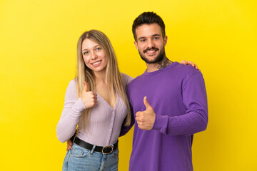 Young couple over isolated yellow background giving thumbs up gesture