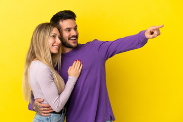 Obraz premium Young couple over isolated yellow background pointing finger to the side and presenting a product