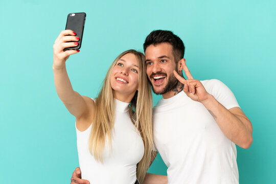 Young couple over isolated blue background making a selfie with the mobile