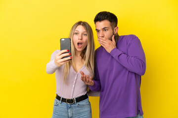 Young couple over isolated yellow background making a selfie with the mobile