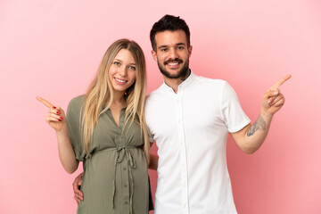 Pregnant woman and man over isolated pink background pointing finger to both sides