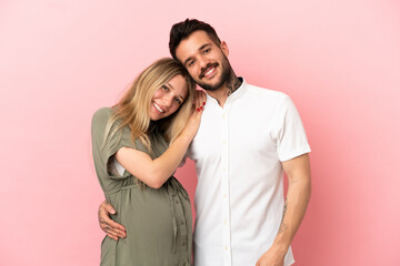 Pregnant woman and man over isolated pink background laughing