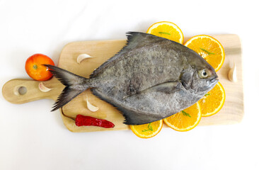 Closeup view of black pomfret fish decorated with fruits and herbs on a wooden pad,white background,Selective focus.