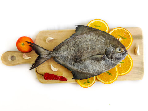 Closeup view of black pomfret fish decorated with fruits and herbs on a wooden pad,white background,Selective focus.