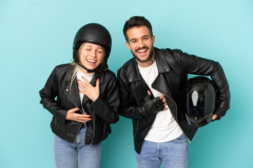 Couple with motorcycle helmet over isolated blue background smiling a lot while putting hands on chest