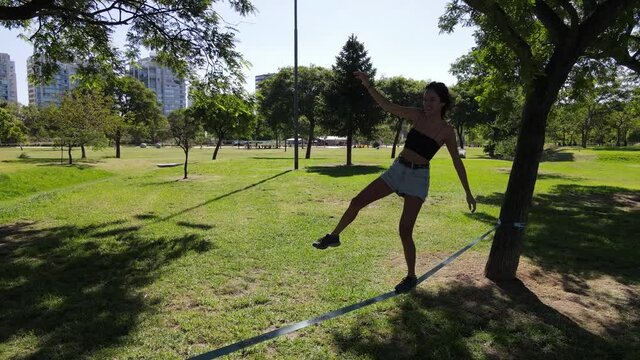 Young happy woman trying to balance on slack line at the park