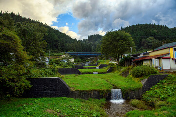 The water weir is surrounded by nature in rural Japan, on a cloudy day in the valley village of Fukushima, a concrete gutter slows water from the mountains