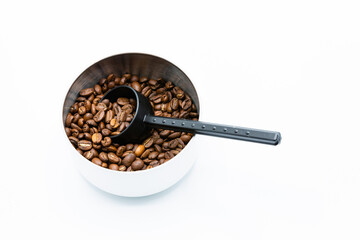 Mixture of different kinds of roasted coffee beans with black plastic spoon in white container on white background. Copy space.
